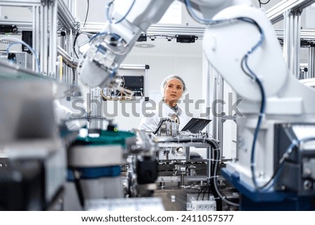 Female engineer controlling production process of modern robotic arm machine in automotive industry. Royalty-Free Stock Photo #2411057577