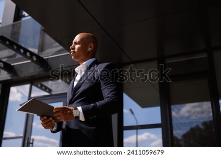 Side view of african american businessman in earphone holding documents near building	