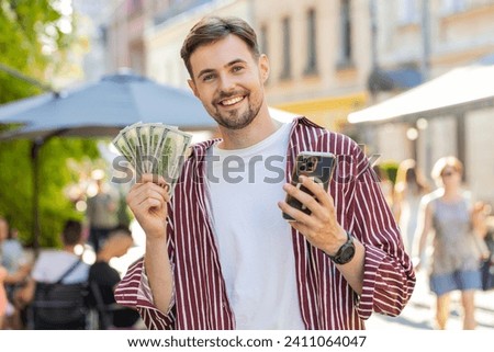 Happy rich bearded man counting holding money dollar cash, use smartphone calculator app, plans to order gifts and food delivery online booking hotel room. Brunette young guy tourist on city street