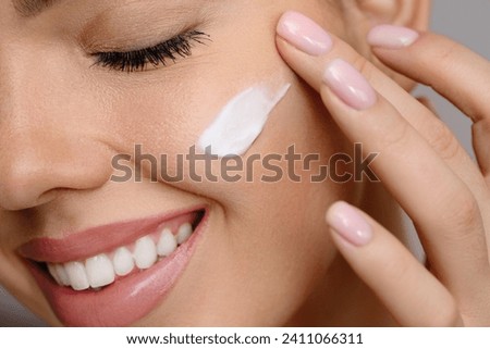 Woman with beautiful face touching healthy facial skin portrait. Beauty close up girl is applying a skincare product. Hydration. Cream smear.  Royalty-Free Stock Photo #2411066311