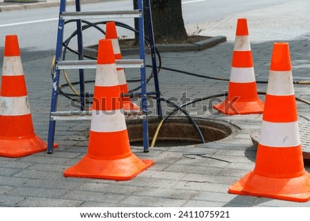 Orange cones installed around the dangerous area on the sidewalk. An open travel hatch. Laying of a new fiber-optic cable in the city network. orange construction cone