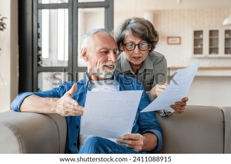 Mortgage loan debt transactions paying bills and documents. Caucasian senior old couple spouses reading marriage contract, doing paperwork, dealing with data at home Royalty-Free Stock Photo #2411088915