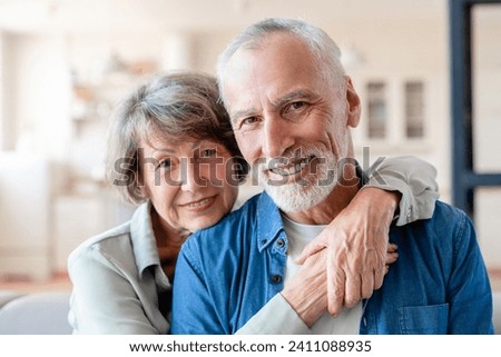 Senior old elderly spouses grandparents couple looking at camera while hugging embracing cuddling together at home. Physical touch - love language