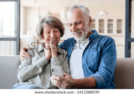 Smart caucasian old elderly senior grandparents couple spouses using cellphone for scrolling social media, online shopping, rentals, remote studies, paying in application at home Royalty-Free Stock Photo #2411088939