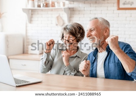 Caucasian senior old elderly couple husband and wife spouses grandparents watching movie, celebrating, winning, victory, cheering the prize from bidding online casino bets with laptop Royalty-Free Stock Photo #2411088965