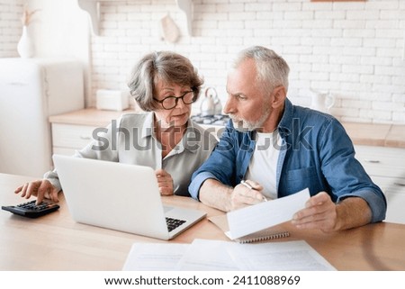 Busy caucasian old elderly senior couple making calculations at home kitchen, checking the document, revising data, information, counting domestic bills and rentals Royalty-Free Stock Photo #2411088969