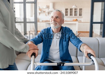 Trust and care. Caregiver caretaker wife helping aiding supporting old elderly senior incapacitated handicapped disabled husband patient with walking frame at home hospice clinic Royalty-Free Stock Photo #2411089007