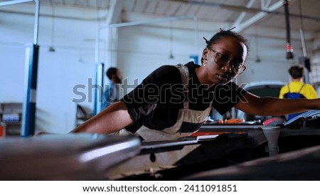 POV shot of precise technician opening car hood in repair shop, using work light to check for damages during maintenance. African american garage worker using professional tool to look inside vehicle Royalty-Free Stock Photo #2411091851
