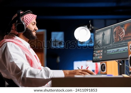 Middle Eastern employee editing video content on multimedia software seen on his computer screen. Side-view shot of male filmmaker working on movie montage edit on the pc monitor.
