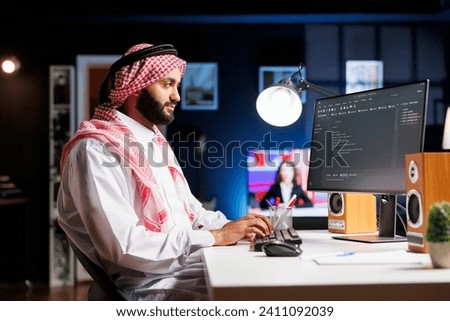 Side-view of Muslim developer writing code on desktop pc, parsing algorithm in a software agency. Using a computer monitor, a Middle Eastern male coder works on a user interface. Royalty-Free Stock Photo #2411092039