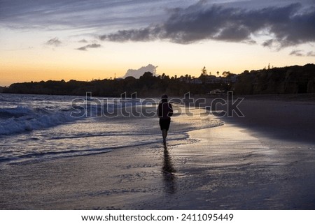 Woman walking on the beach at sunset in the Algarve, Portugal.