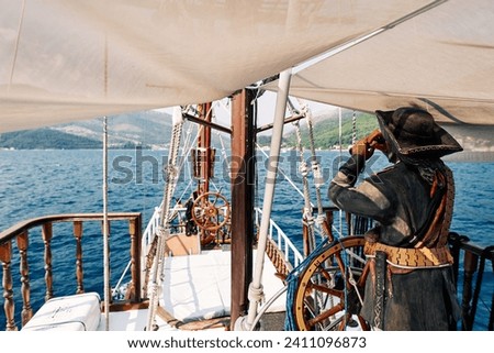 Figure of a pirate with a telescope stands at the helm of a sailboat sailing on the sea. Back view