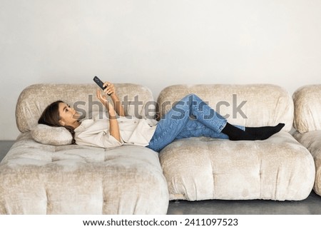Close up of a relaxed girl using a smart phone lying on a sofa in the living room at home with a cozy background