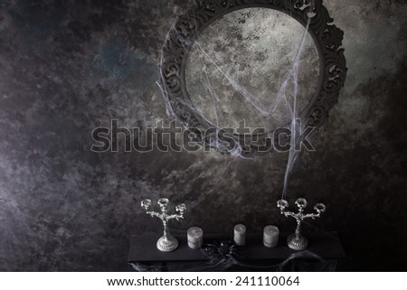 High Angle View of Decorative Round Frame Above Candles and Candelabras on Eerie Cobweb Covered Mantle in Haunted House Setting