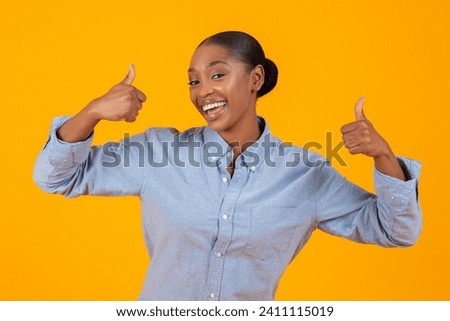 I like it. Portrait Of Cheerful Black Woman In Casual Gesturing Thumbs Up Symbol, Approving Great Offer, Posing Wearing Denim Shirt Standing Over Yellow Background In Studio