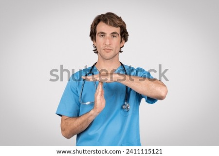 Attentive male nurse in blue scrubs with stethoscope around his neck making timeout hand gesture, indicating need for break or attention Royalty-Free Stock Photo #2411115121