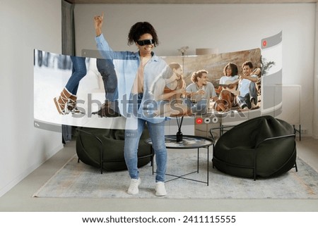 Tech-savvy young black woman connects with friends on picnic through virtual screen, experiencing digital camaraderie via VR headset at home Royalty-Free Stock Photo #2411115555