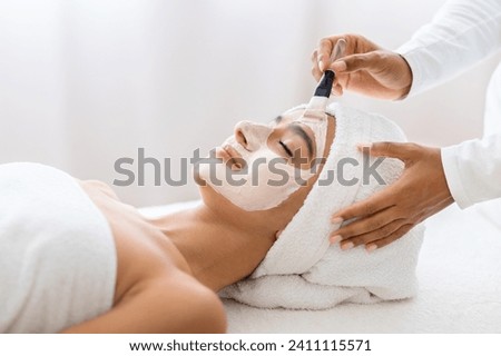 In a moment of tranquility, young indian woman experiences the luxury of a professional facial mask treatment, enhancing her skin's radiance. Day at spa, beauty treatment Royalty-Free Stock Photo #2411115571