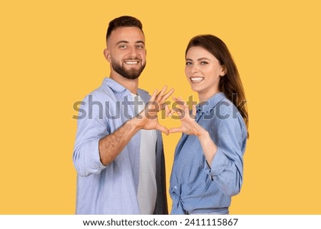 Smiling man and woman affectionately forming heart shape with their hands, symbolizing love and connection, against warm yellow background