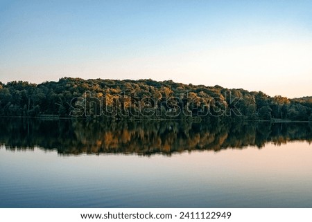Landscape of peaceful area covered with trees and reflecting in still water Royalty-Free Stock Photo #2411122949