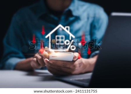 Businessman use smartphone with virtual home icon and down arrow for economical real estate and lower mortgage interest rates. Reduced prices for rental housing, Demand for home purchases decreases. Royalty-Free Stock Photo #2411131755