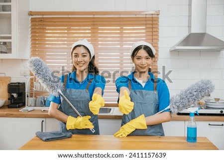 Portrait of two Asian housekeepers on kitchen counter with duster foggy spray and rag. Reflecting efficient housework teamwork and hygiene. Clean portrait two uniform maid working smiling employee. Royalty-Free Stock Photo #2411157639