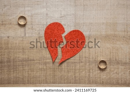 Divorce concept. Broken red paper heart and wedding rings on wooden background. Royalty-Free Stock Photo #2411169725