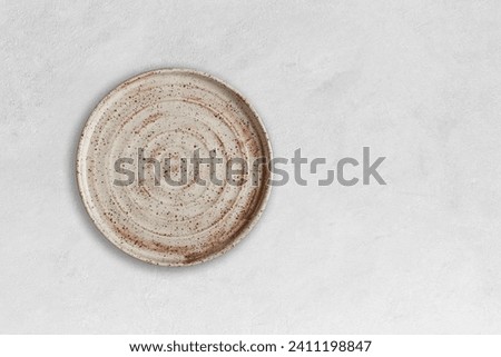 Handmade empty ceramic plate top view with copy space on grey concrete table. Minimalism. Eco friendly ceramics handcraft tableware. Royalty-Free Stock Photo #2411198847