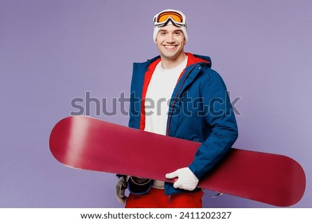 Side view smiling happy fun man wear warm blue windbreaker jacket ski goggles mask hat hold snowboard look camera spend extreme weekend winter season in mountains isolated on plain purple background Royalty-Free Stock Photo #2411202327
