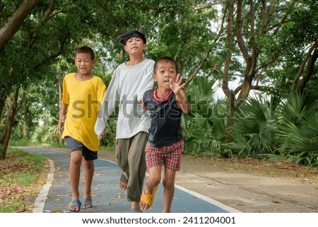 Group of three Asian boys were running fast without care is causing an accident or falling in danger on the road in the park on forest background.