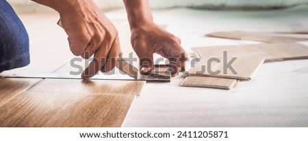 A technician is cutting luxury vinyl floor tiles with a cutter to lay the floor before placing it on the leveling foam. Royalty-Free Stock Photo #2411205871