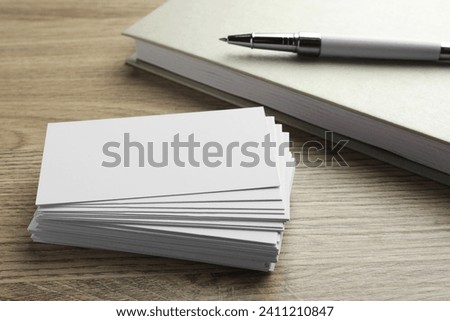 Stack of blank business cards, notebook and pen on wooden table. Mockup for design