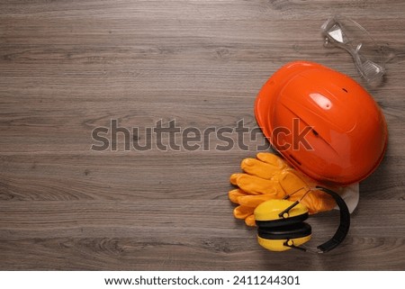Hard hat, gloves, goggles and earmuffs on wooden table, flat lay with space for text. Safety equipment Royalty-Free Stock Photo #2411244301
