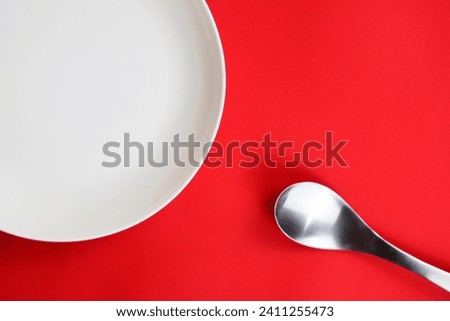 Empty white plate and spoon on red background