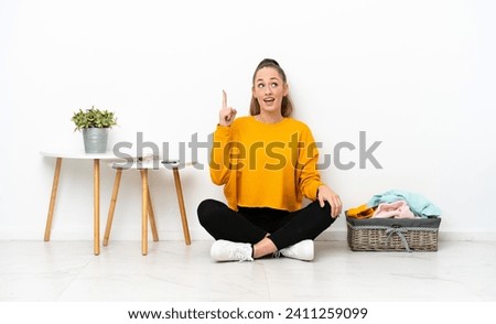 Young caucasian woman folding clothes sitting on the floor isolated on white background intending to realizes the solution while lifting a finger up