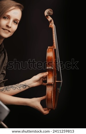 Holding the violin gently, the artist's tattooed arm suggests a blend of classical finesse and modern expression Royalty-Free Stock Photo #2411259813