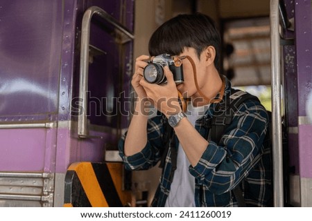 A handsome young Asian man traveler backpacker is taking pictures with his camera while getting off the train. Vacation in Asia, solo trip, people and transportation concepts