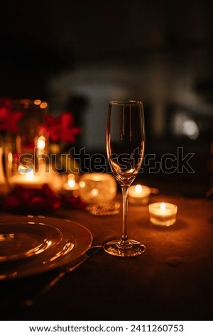 Candlelight date in restaurant. Champagne glasses, bouquet flowers. Romantic dinner setup at night. Table setting for couple, Valentine's Day evening, burning candles for surprise marriage proposal. Royalty-Free Stock Photo #2411260753