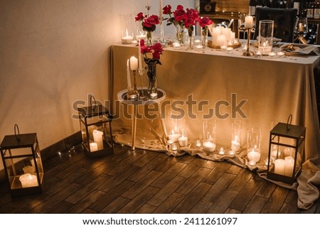 Candlelight date in restaurant. Glasses with wine, bouquet flowers. Romantic dinner setup at night. Table setting for couple, Valentine's Day evening, burning candles for surprise marriage proposal. Royalty-Free Stock Photo #2411261097