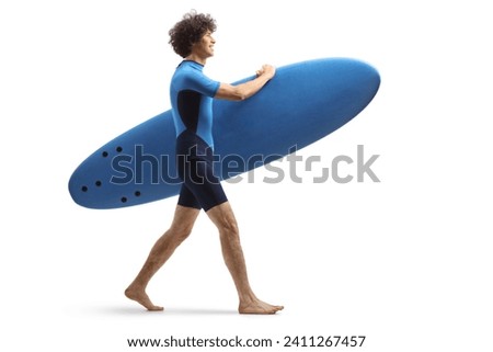 Full length profile shot of a guy in a wetsuit walking and carrying a surfboard isolated on white background