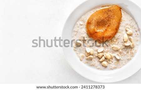 Close up view of oat porridge with caramelized pear and peanut in bowl over white background with copy space. Top view, flat lay