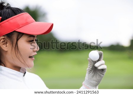 Portrait head shot of young asian female golfer holding the golf ball at the course over white sky background,