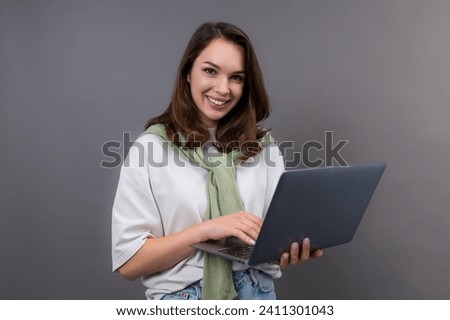 A smiling student with a laptop looks into the camera on a gray isolated background