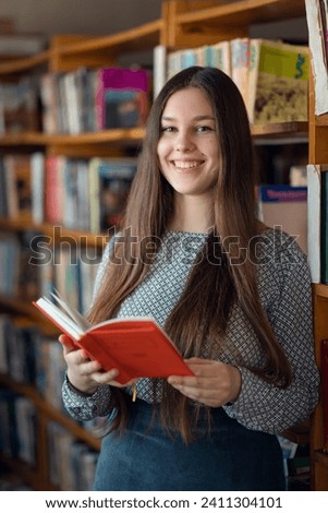 Smiling female college student reading a book in library. Portrait of cheerful girl in university library