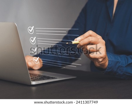 Quality control assurance of the ISO concept. A businessman in a navy blue shirt using an electronic pen to tick the correct sign mark in an online document checklist while sitting at the desk