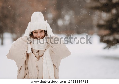 Happy smiling young woman portrait dressed coat scarf hat and mittens enjoys winter weather at snowy winter park Royalty-Free Stock Photo #2411314781