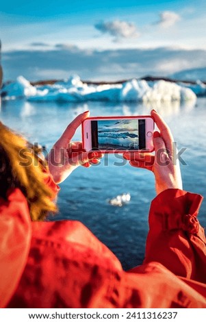 Woman taking a picture by smartphone of a blue iceberg in ice lagoon jokulsarlon at Iceland. Woman taking photograph of beautiful Icelandic nature in Vatnajokull. Travel theme