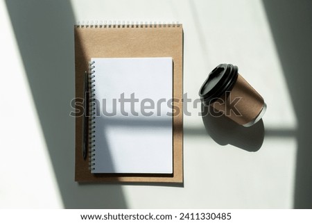 blank notepad in sunlight with a pen on the table and with a glass of coffee. view from above.
