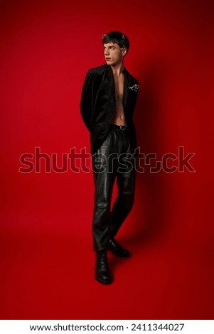young man in stylish outfit with flowers in hair and pocket of velvet blazer posing on red backdrop