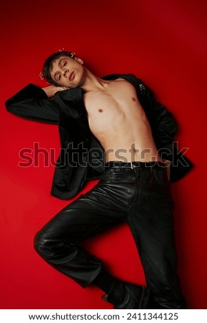 top view of male model in jacket and leather pants lying and looking at camera on red background